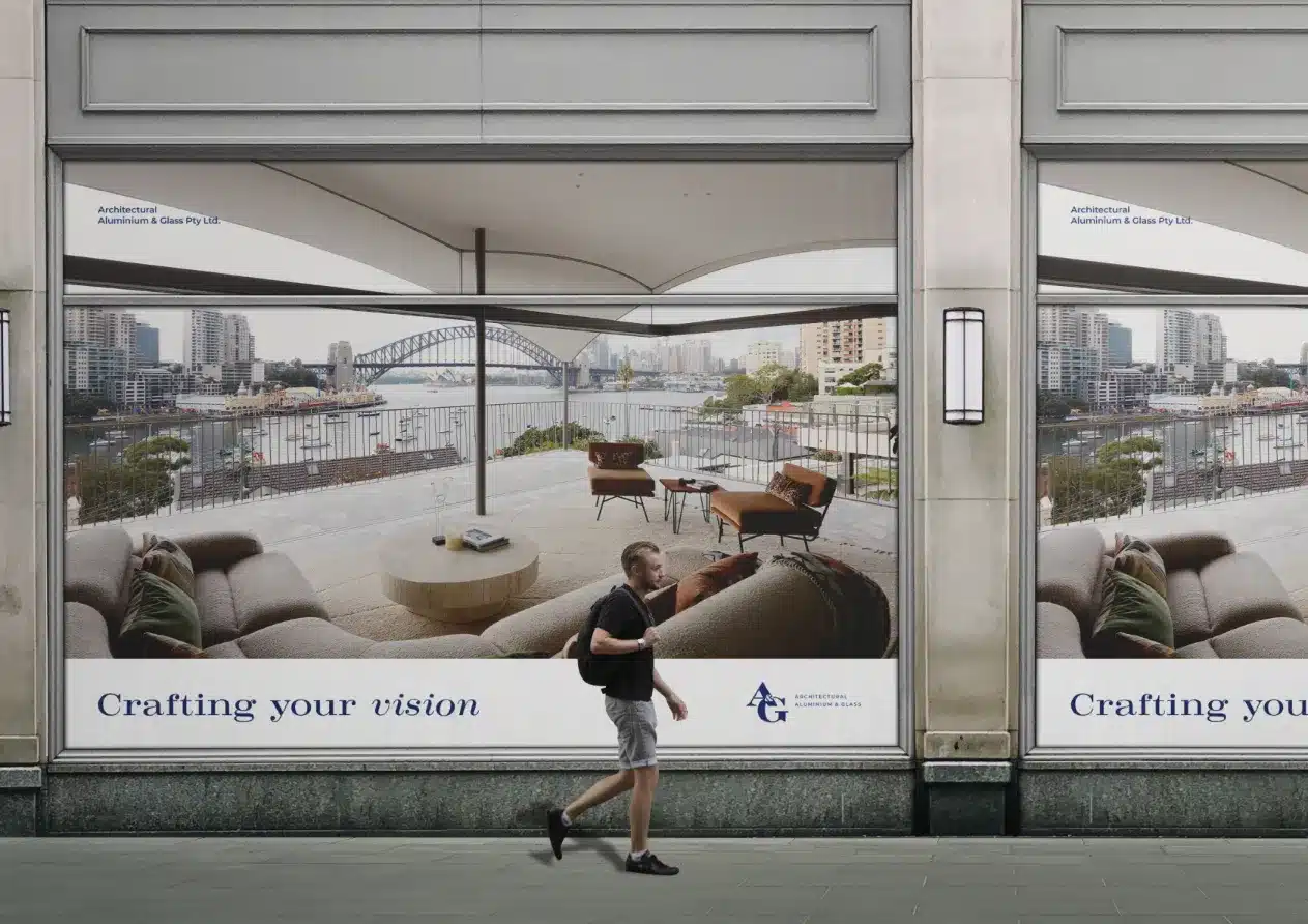 A man strolls by a building adorned with large A&G posters showcasing a luxurious balcony view of a cityscape featuring an iconic bridge.