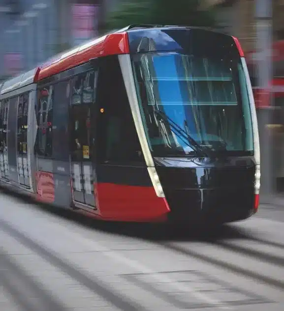 A sleek modern tram in red and black glides along a city street, surrounded by the blurred buildings and lights, offering a glimpse into the vibrant future of urban transit in 2024.