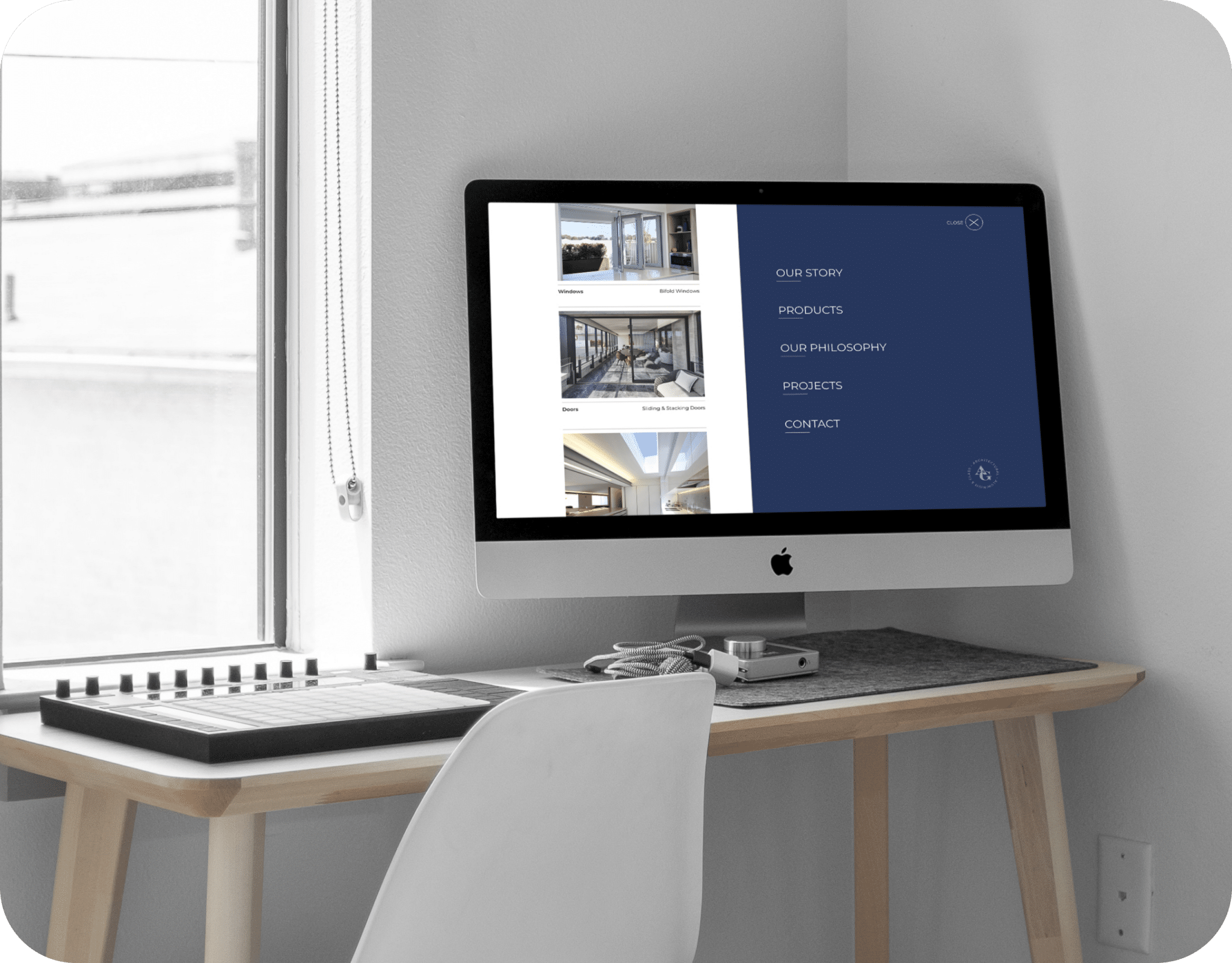 A computer displaying the A&G website menu is on a wooden desk next to a MIDI controller, with a window in the background.