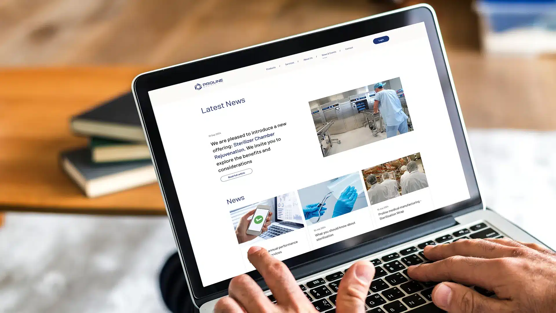 A person is using a laptop showcasing a website with sections for the latest news, featuring images of medical equipment in laboratory settings and digital devices. Books fill the background, subtly emphasizing the vital role Proline Medical plays in advancing healthcare services.