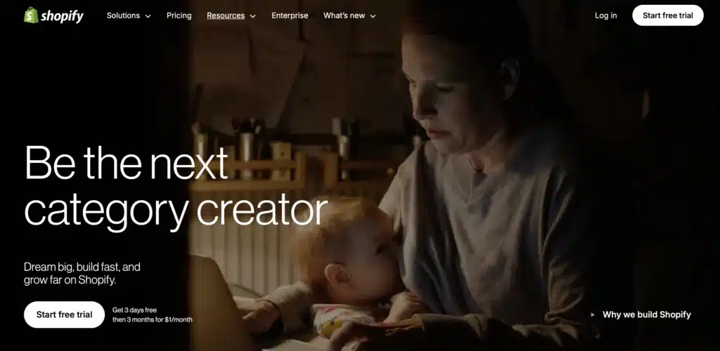 A woman multitasks on a laptop with her child in her lap. The text reads, "Be the next category creator" and highlights Shopify's free trial offers, ideal for Australian businesses looking to harness the perfect eCommerce CMS.