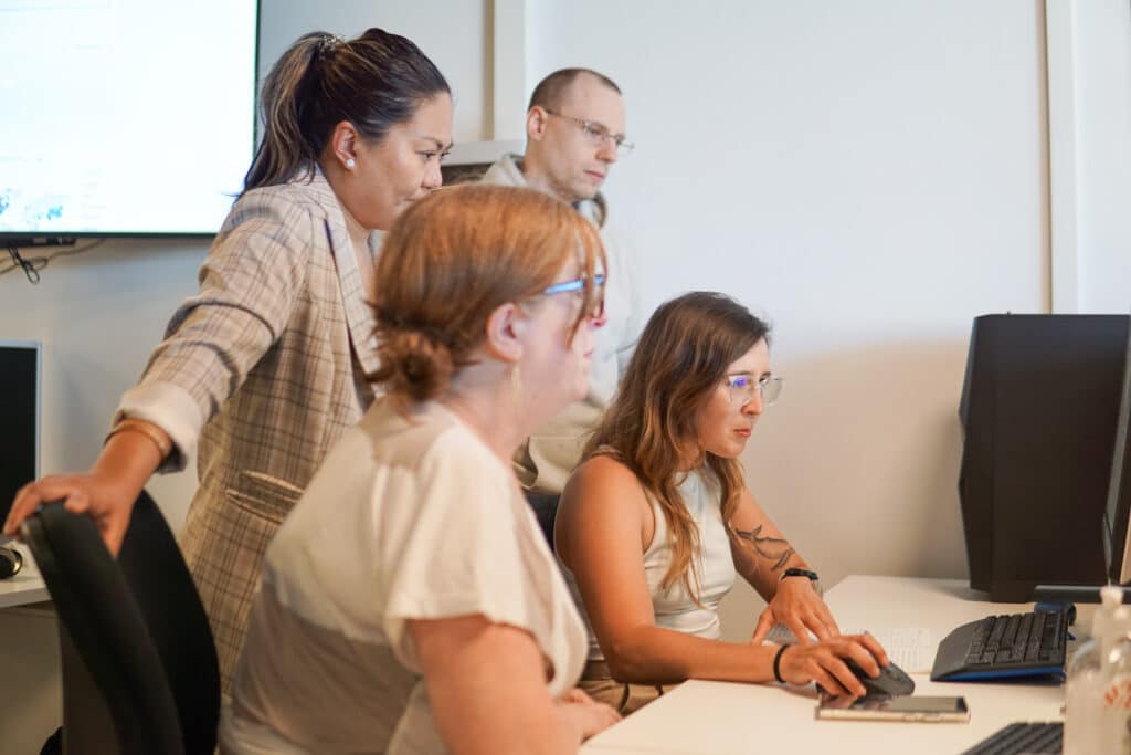 Four people in an office setting focus on a computer screen, with one person typing while the others observe—capturing the collaborative spirit behind Spark Interact's 2025 Australian Web Award entry.