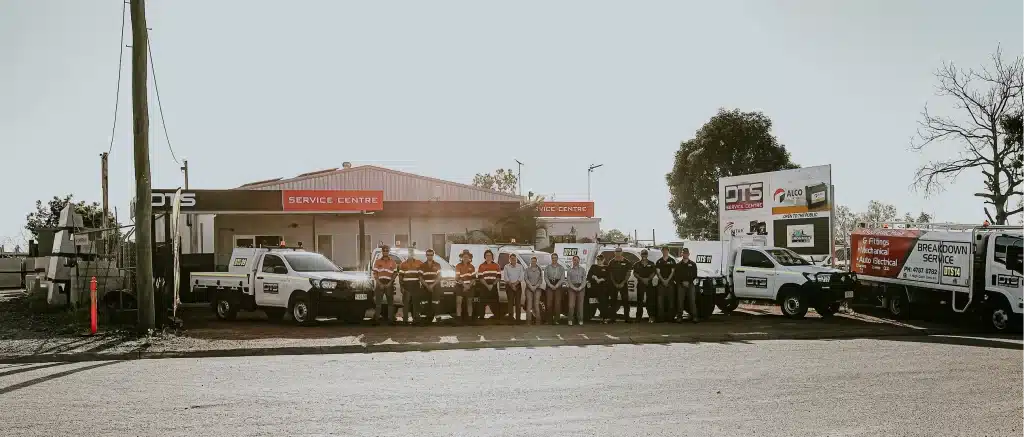 A group of people stands in front of a Commercial Powerhouse Service Center building and several branded utility vehicles in a parking lot.