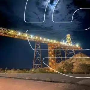 A large illuminated mining conveyor structure stands over piles of earth at night, with a cloudy moonlit sky in the background and graphic lines overlaid, symbolizing the importance of avoiding outdated documents in business Capability Statement Audits.