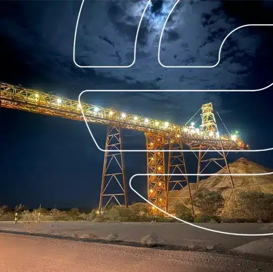 A large illuminated mining conveyor structure stands over piles of earth at night, with a cloudy moonlit sky in the background and graphic lines overlaid, symbolizing the importance of avoiding outdated documents in business Capability Statement Audits.
