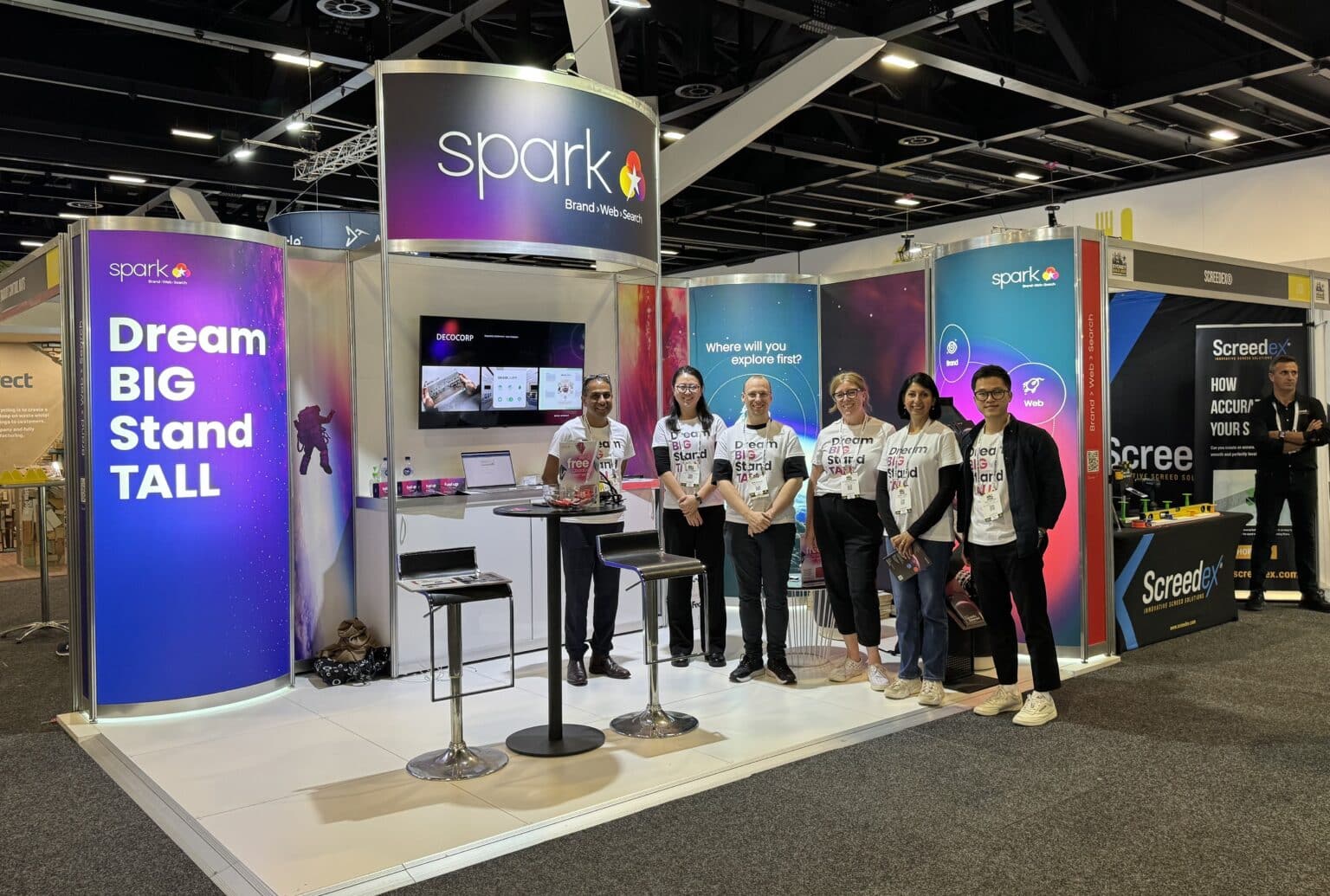 The Spark team stand in front of an exhibition booth at a Sydney Build Expo 2024, featuring display screens, branded banners, and colorful signage—demonstrating how Booth to Business strategies can maximise expo ROI.