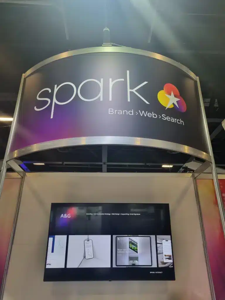 A business expo booth with a sign reading "spark Brand › Web › Search" above a monitor displaying digital design mockups, designed to maximize Expo ROI.