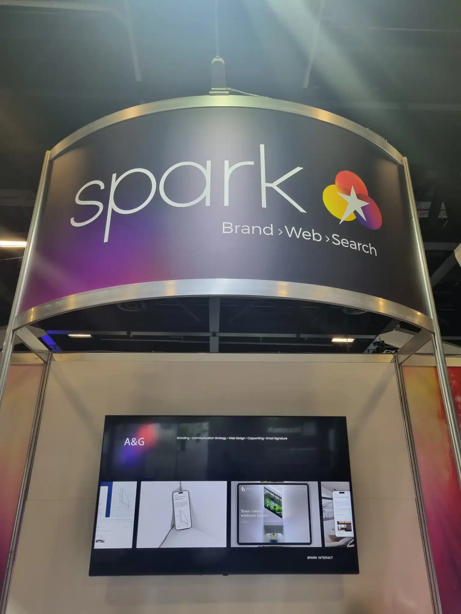 A business expo booth with a sign reading "spark Brand › Web › Search" above a monitor displaying digital design mockups, designed to maximize Expo ROI.