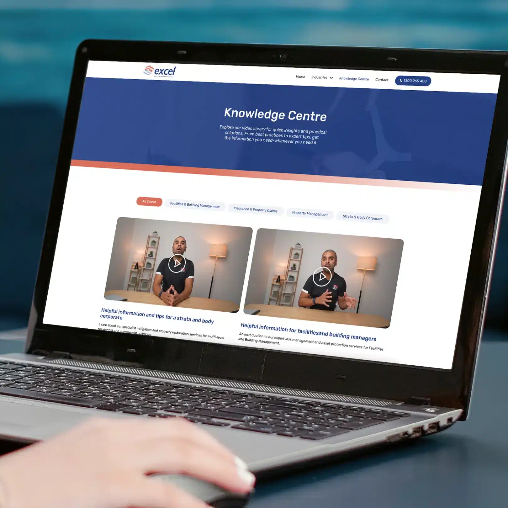 A person uses a laptop displaying the Excel Knowledge Centre webpage, featuring informational videos, navigation tabs, and the company's logo as part of its digital identity.