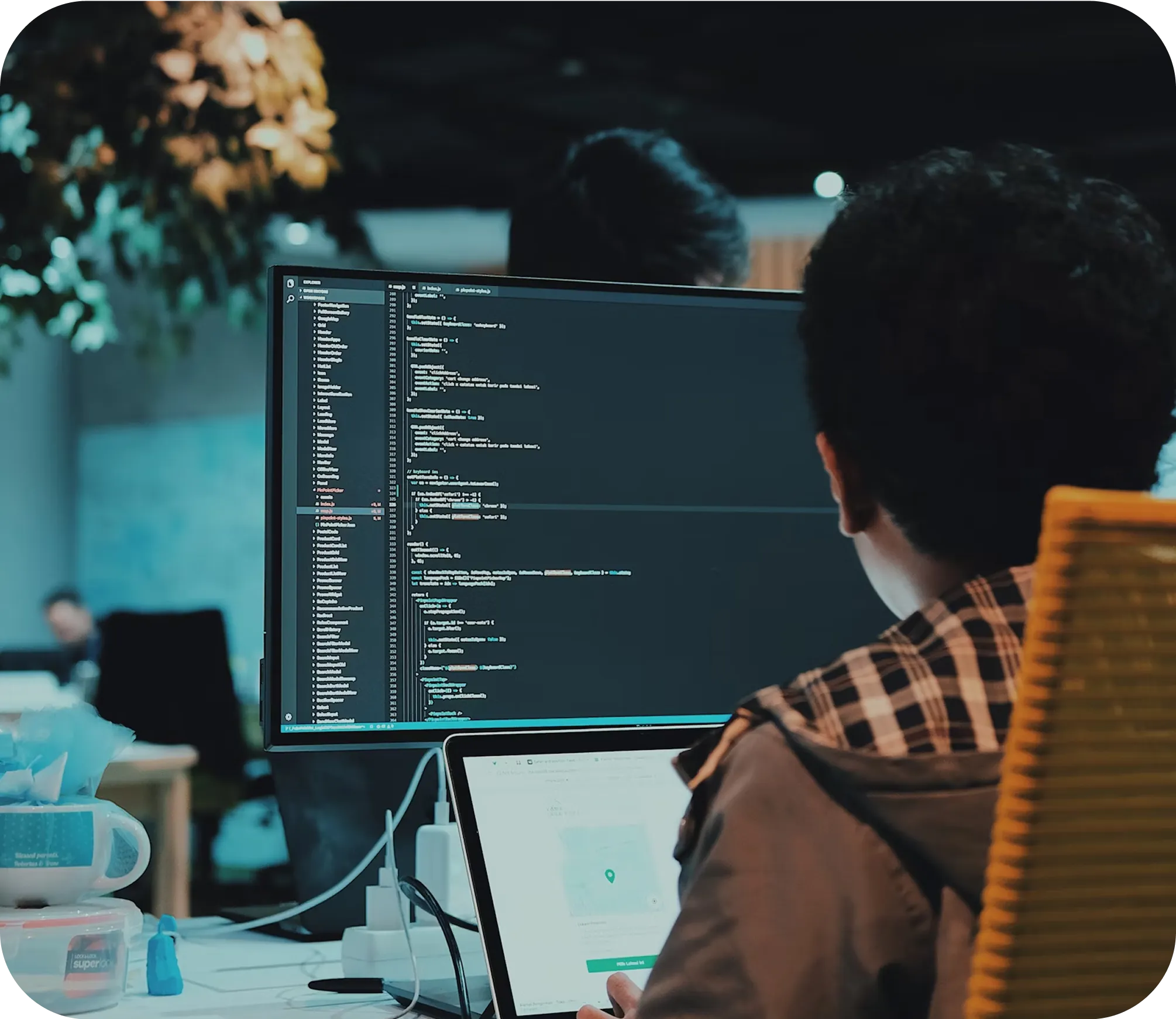 A professional sits at a desk in an office, working on code for enterprise solutions on a large monitor, while referencing a map application on their laptop—an ideal setting for an AI automation agency or growing SME.