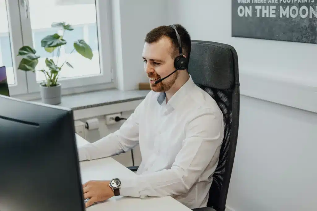 A man wearing a headset and white shirt sits at a desk working on a computer in a modern office, focusing on AI optimisation tasks.