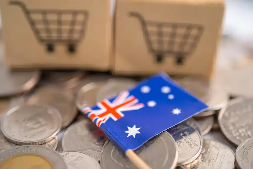 A small Australian flag on coins with cardboard boxes featuring shopping cart symbols in the background, perfect for illustrating an SEO Content Strategy or showcasing a WooCommerce Developer Sydney’s e-commerce expertise.