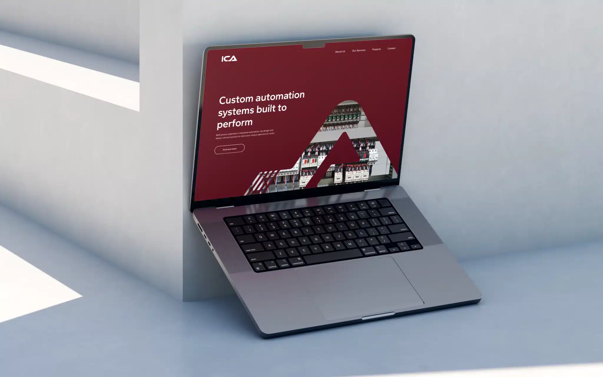 A laptop leaning against a white wall displays a website with a maroon background and the text "Custom automation systems built to perform," highlighting Industrial Controls Australia’s commitment to brand elevation.