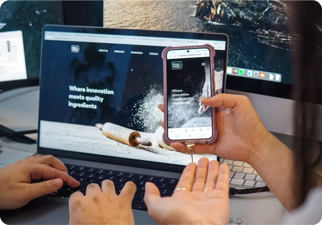 Two people view a baking-related Home Page on a laptop and smartphone, both displaying the same webpage; baking tools and flour are shown on the website banner, reflecting fresh trends for 2025.