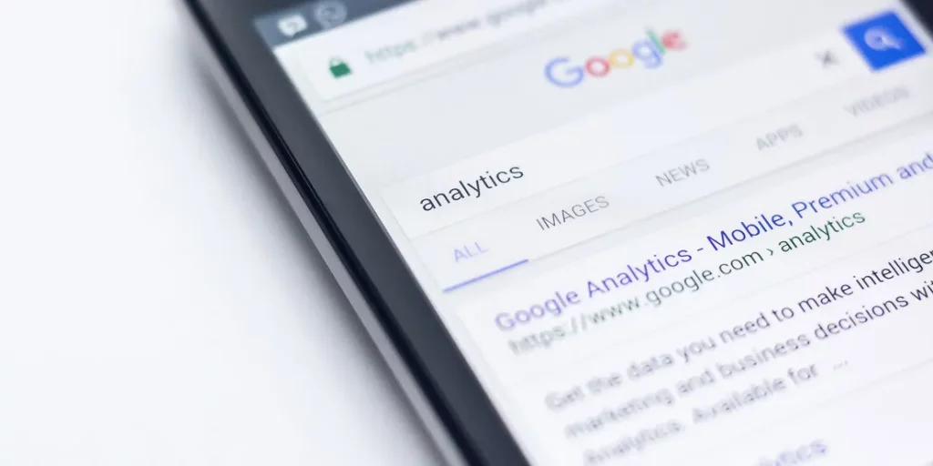 A smartphone displays a Google Search Service Page for the keyword "analytics," showing links and snippets below the search bar.