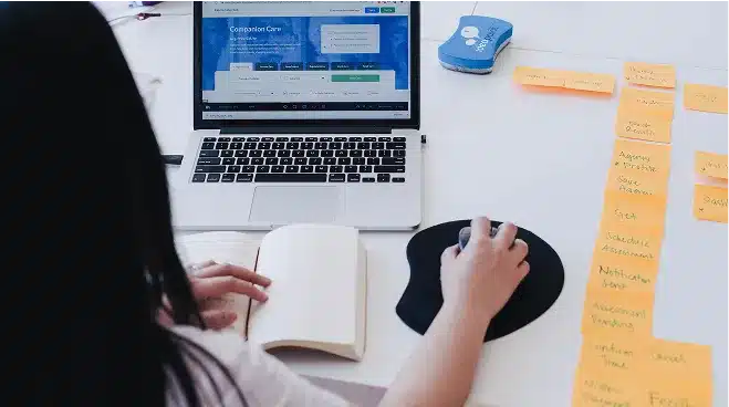 Person working at a desk with a laptop, open notebook, and mouse, using sticky notes organized in a column to plan Web Services projects for 2025.