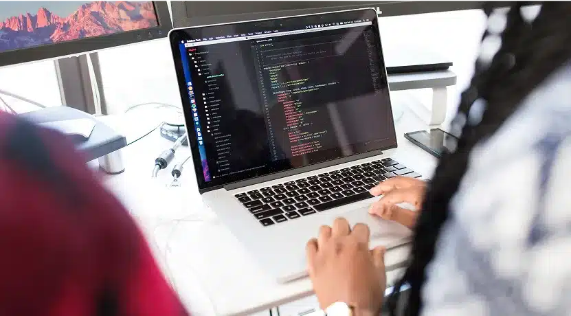 Two people sit at a desk, one typing on a laptop displaying lines of code for Web Services, with monitors and office supplies visible in the background, setting the scene for a productive 2025.