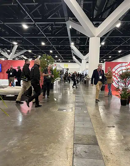 Attendees stroll through a spacious, modern convention center hallway at Supply Nation Connect 2025, surrounded by concrete floors, vibrant plants, and red displays celebrating supplier diversity in the background.