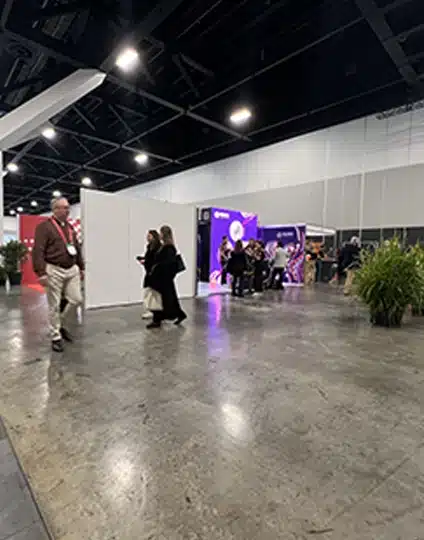 People walk and gather near booths in a convention center with polished concrete floors and bright overhead lighting at Supply Nation Connect 2025, a key event for the supply chain community.