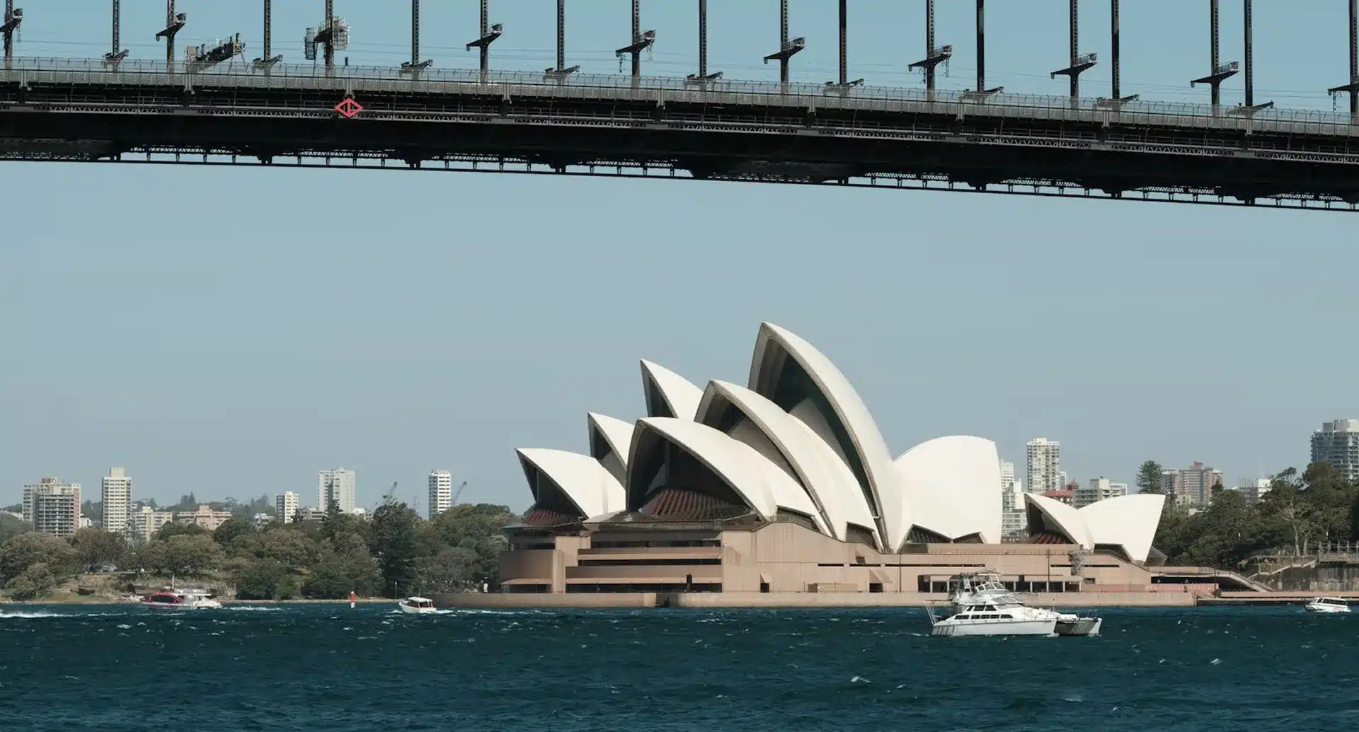 The Sydney Opera House and city skyline are seen from across the harbor, with part of the Sydney Harbour Bridge visible at the top. Boats glide on the water in the foreground, creating a picturesque scene worthy of any Testimonial Archive.