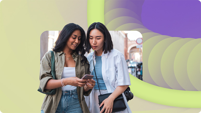 Two women stand together outdoors, looking at a smartphone, as abstract shapes form a vibrant backdrop—highlighting how AI and Microsoft Advertising can boost ROI in the digital world.